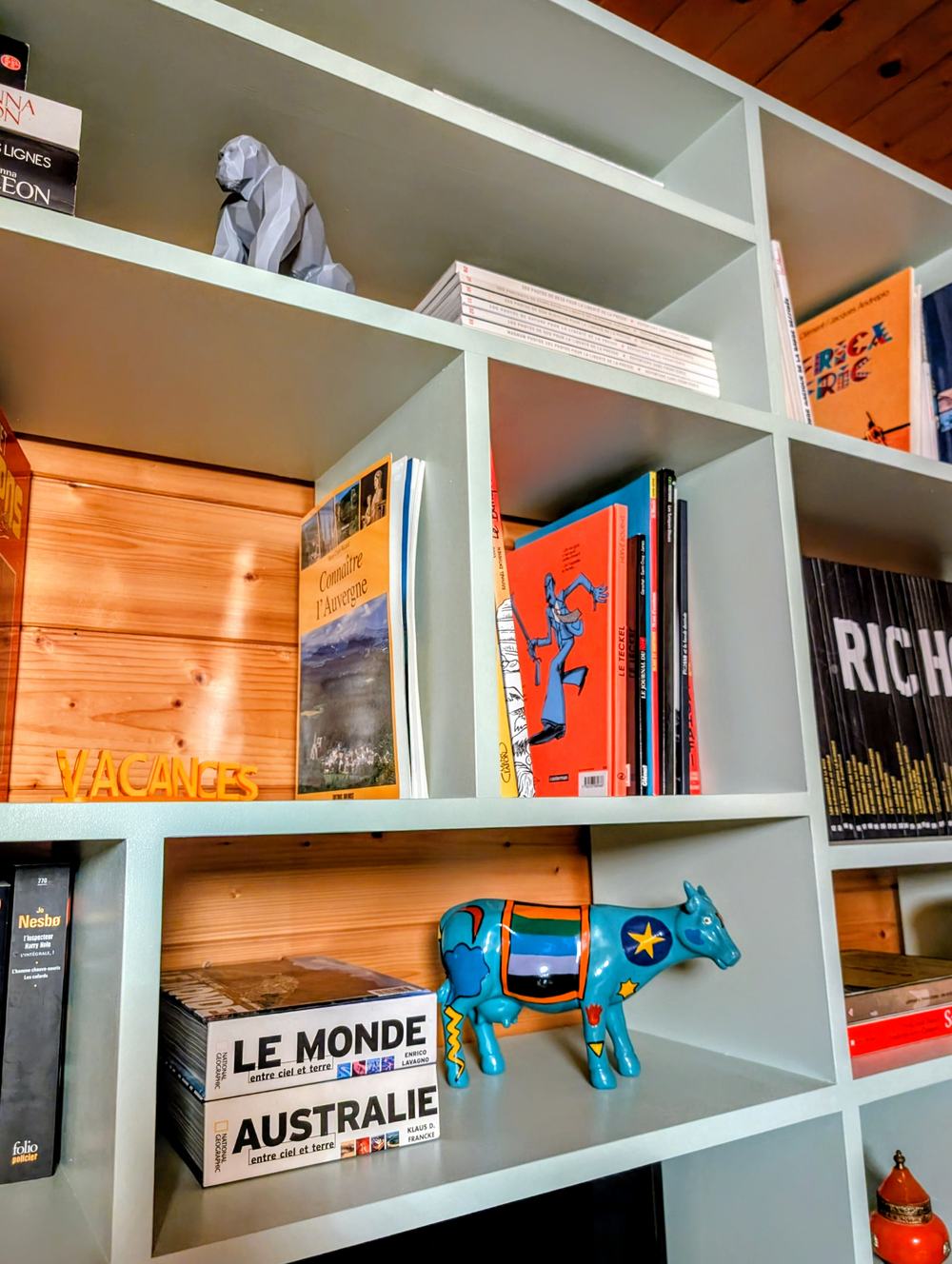 Détail de la bibliothèque du salon, livres illustrés et vache décorative bleue