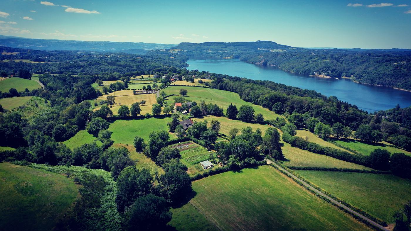 Vue aérienne des prairies et bocages de l'Artense descendant vers le lac
