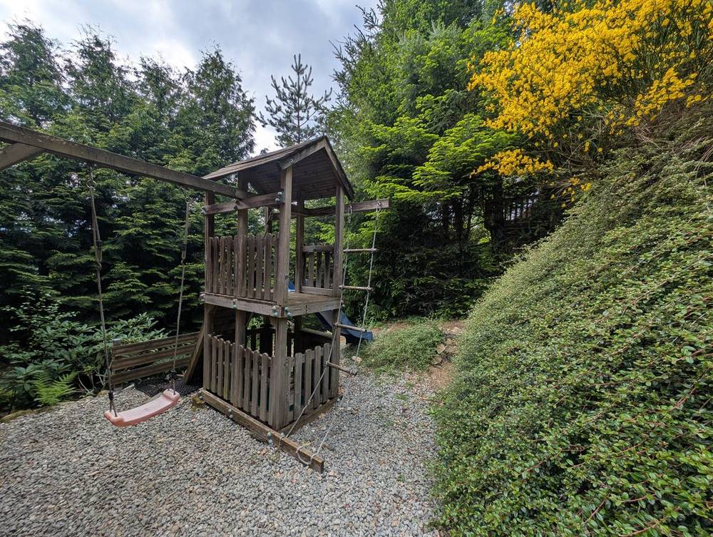 Le portique du jardin : balançoire, cabane et échelle de corde, entouré de sapins