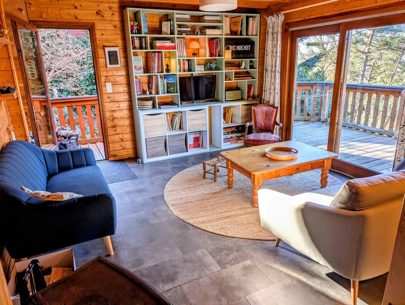 Le salon du chalet, sa grande bibliothèque vert d'eau, la télévision et la baie vitrée ouvrant sur la terrasse