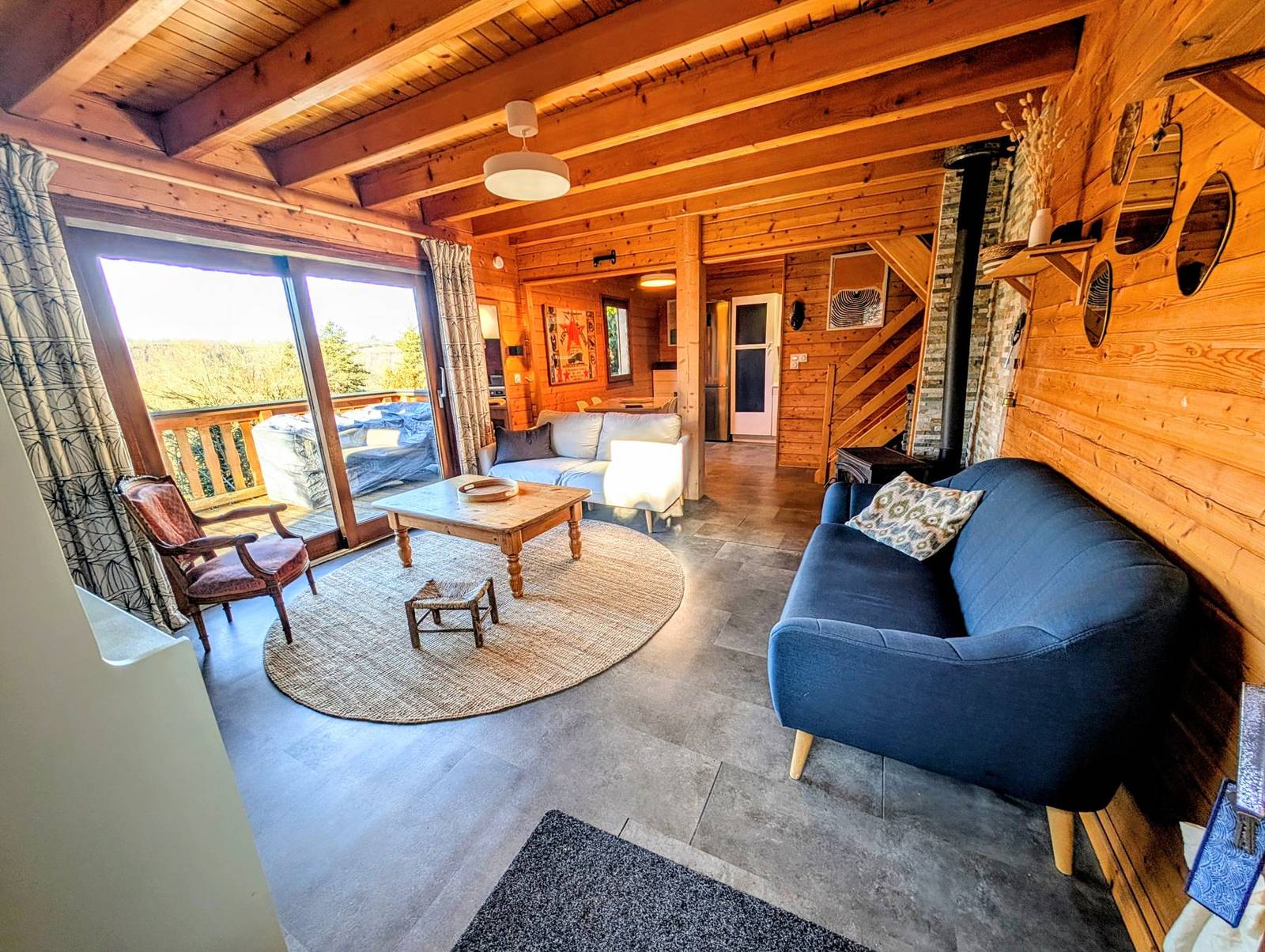 Le salon du chalet, murs et plafond en bois, poêle, canapés et grandes baies vitrées ouvrant sur la terrasse